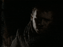 a man with a scarf around his neck is standing in the dark .