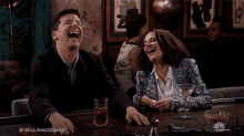 a man and a woman are laughing at a bar with #willandgrace written on the bottom of the image