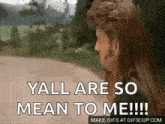 a man with long hair is standing on a dirt road and saying `` yall are so mean to me ! ''