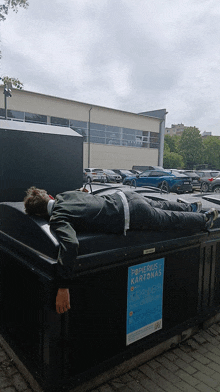 a man is laying on top of a dumpster that says papieriuse kartonas on it