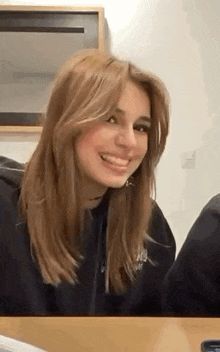 a young woman with long brown hair is smiling while sitting at a table .
