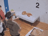 a man standing in front of a bed with pizza on it and the number 2 on the wall