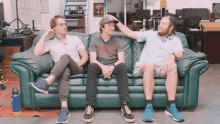 three men are sitting on a green couch and one of them has a shirt that says never give up on it
