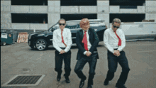 three men in suits and ties are dancing in a parking lot in front of a building