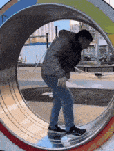 a man in a gray jacket is walking through a metal tube in a park