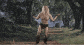 a man without a shirt is holding a sword in a field