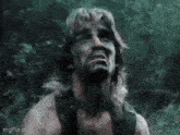 a man with long hair and a beard is standing in the woods and making a funny face .