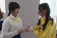 two girls are shaking hands and one has a yellow sweatshirt on that says ' i love you ' on it