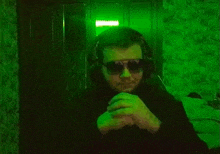 a man wearing headphones and sunglasses is sitting in front of a green wall .