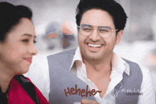 a man wearing glasses is smiling next to a woman who is laughing and the word henehe is visible