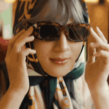 a woman wearing sunglasses and a scarf around her head is talking on a cell phone