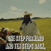 a man in a cowboy hat stands in a field next to a piano with the words one step forward and ten steps back