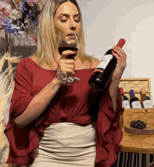 a woman in a red off the shoulder top is holding a bottle of wine