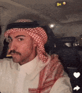 a man wearing a head scarf and a white shirt is in a car