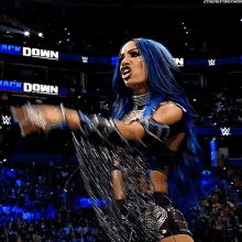 a woman with blue hair is standing in front of a crowd in a wrestling match .