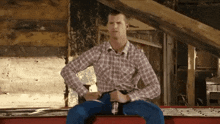 a man in a plaid shirt and blue jeans sits on a red box