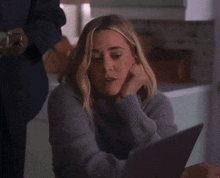 a woman in a gray sweater is looking at a tablet
