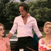 a man in a pink shirt stands next to two women