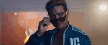 a man wearing sunglasses and a blue jacket is standing in front of a wall .