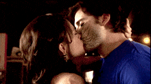 a man in a blue shirt kisses a woman in a black dress