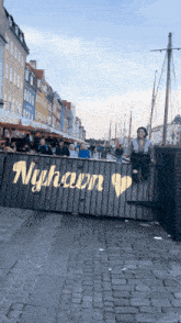 a woman sits on a wooden fence in front of a sign that says nyhavn