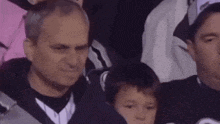 a group of people are sitting in a stadium watching a game and one of them is holding a child .