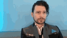 a man with a beard is wearing a suit and tie and has the letters rk800 on his jacket .
