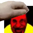a hand is putting a hat on a man 's head with a red face .