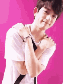 a young man in a white t-shirt is standing in front of a pink wall .