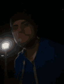 a man is smoking a cigarette in the dark while wearing a beanie and a blue jacket .