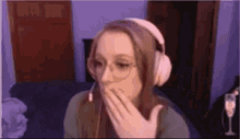 a woman wearing headphones and glasses is covering her mouth while sitting on a couch .