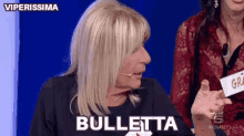 a woman with blonde hair is talking into a microphone and says bulletta