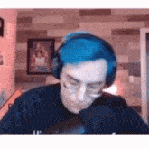 a man with blue hair is wearing headphones and glasses while talking into a microphone .