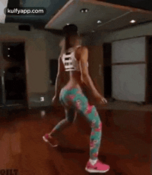 a woman is dancing in a gym wearing floral pants and a white tank top .