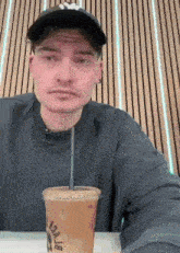 a man is sitting at a table drinking an iced coffee with a straw .