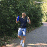 a man is walking down a brick path holding a blue bottle and a blue cup