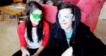 two people wearing masks are sitting next to each other on a couch