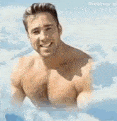 a shirtless man is smiling while sitting in a bathtub surrounded by clouds .