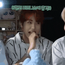a man in a striped shirt is eating a blue stuffed animal with korean writing above him