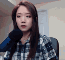 a woman in a plaid shirt is sitting in front of a blue microphone