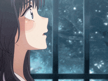 a close up of a girl looking out a window with snow falling