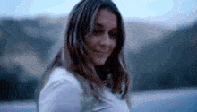 a woman is smiling and looking at the camera while standing in front of a lake .