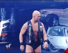 a man in a black vest with the word austin on it is standing in front of a pile of cars .