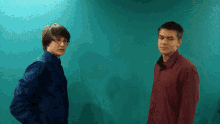 two men standing next to each other in front of a teal wall