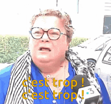 a woman wearing glasses and a scarf is talking into a microphone and says c'est trop