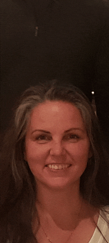 a woman with long hair is smiling and wearing a necklace
