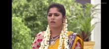 a woman in a yellow sari with flowers in her hair is standing in front of a plant .