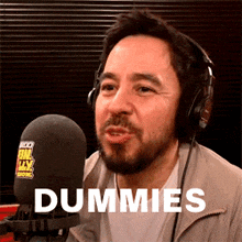 a man wearing headphones is talking into a microphone and the word dummies is on the screen behind him