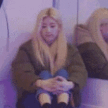 a woman with long blonde hair is sitting in a chair with her hands folded in front of her face .