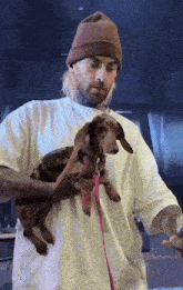 a man wearing a beanie is holding a small dog on a leash